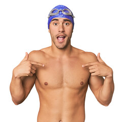 Young Hispanic man with swim gear surprised pointing with finger, smiling broadly.