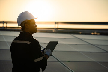 A man wearing a hard hat and safety glasses is holding a tablet in his hand. He is looking up at...