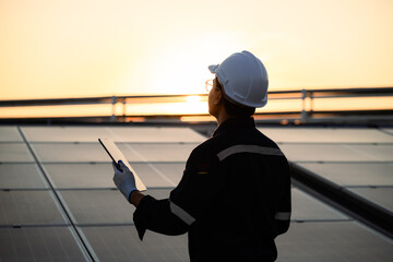 A man wearing a hard hat and safety glasses is holding a tablet while standing on a solar panel