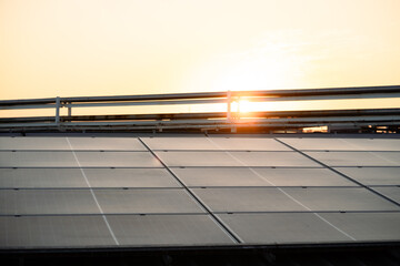 A solar panel array is seen in the sun. The sun is setting in the background. The solar panels are on a roof. Concept: Renewable energy, clean technology, electric energy