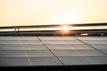 A solar panel array is seen in the sun. The sun is setting in the background. The solar panels are...