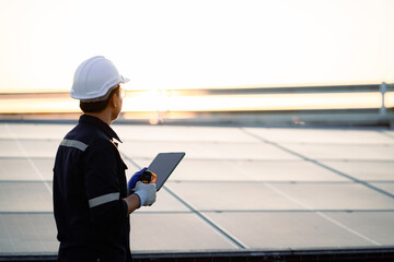 A man wearing a hard hat and safety glasses is holding a tablet while standing on a solar panel....