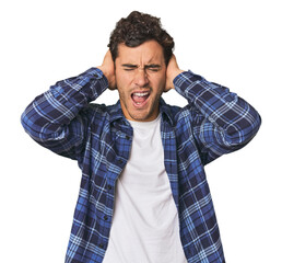 Young Hispanic man in studio covering ears with hands trying not to hear too loud sound.