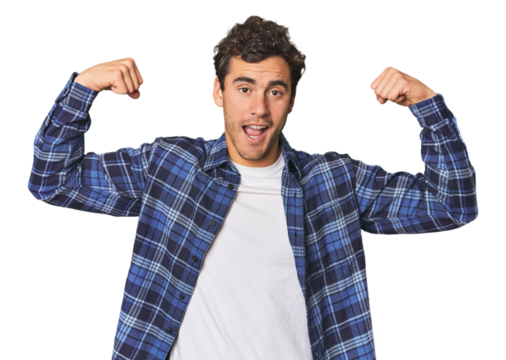 Young Hispanic man in studio showing strength gesture with arms, symbol of feminine power