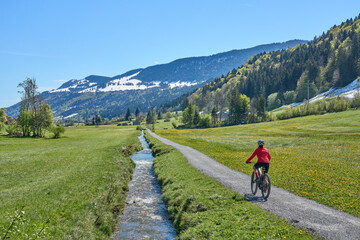 active senior woman riding her electric mountain bike on a sunny day in  spring with Dandelion...