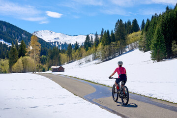 smiling senior woman riding her electric mountain bike on a sunny day in early spring in the...