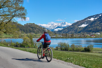 nice senior woman riding her electric mountain bike in springtime at lake Alpsee near Immenstadt,...