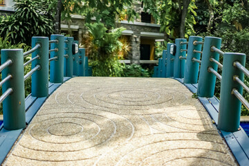 A stable bridge with circle wave pattern stone floor and metal railing for crossing over the pool to the other area in the garden of the resort. Shadow of plants and trees on the bridge.