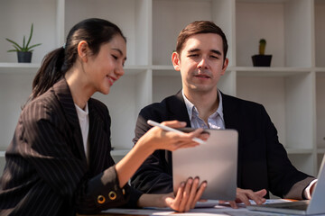 Team of partner business man and business woman discussing project on laptop and tablet sitting at table in office. Two colleagues of professional business people working together
