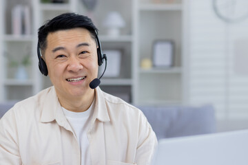 Friendly Asian male professional using a headset in a modern home office setting, looking cheerful...