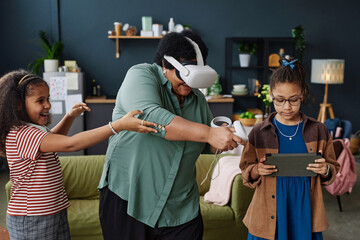 Waist up portrait of modern African American grandmother playing VR game with two girls at home