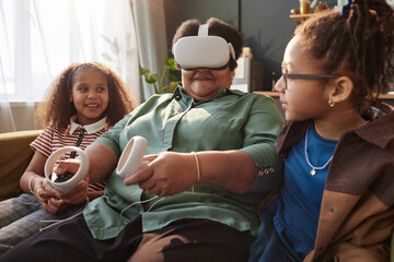 Portrait of African American grandmother wearing VR headset with two little girls sitting on couch at home