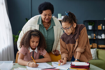 Portrait of two Black girls drawing pictures together with grandmother watching at home