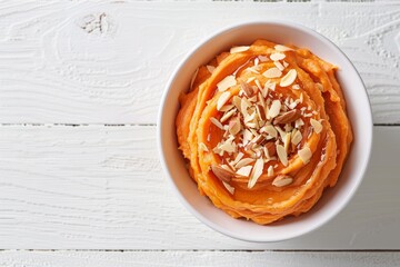 Top view of vanilla bean whipped sweet potatoes with maple syrup and almond flakes in a white bowl on a white wooden table flat lay with empty space