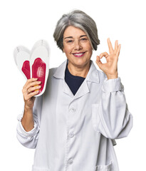 Caucasian mid-age female podiatrist holding insole cheerful and confident showing ok gesture.