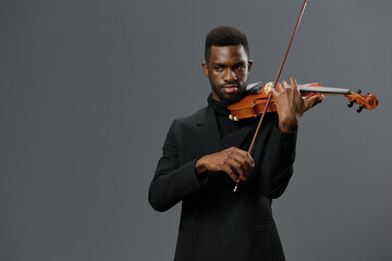 African American man in black suit playing violin on gray background in elegant musical performance portrait