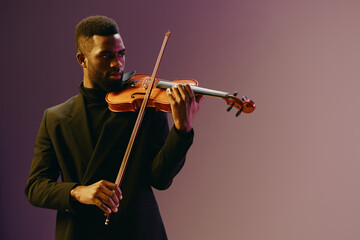 Elegant African American Man in Black Suit Playing Violin Against Purple Background in Studio...