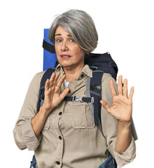 Caucasian mid-age female with hiking gear rejecting someone showing a gesture of disgust.
