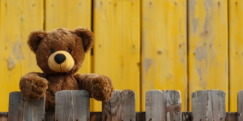 Brown teddy bear climbing on old wooden fence with yellow wood background