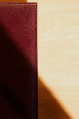 The cover of a burgundy leather notebook is half hidden in the shadow, an office notebook, an expensive office notebook in semi-shadow, vertical shot