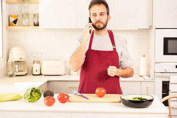 A man in a red apron is talking on a cell phone while preparing food. The kitchen is well-equipped...