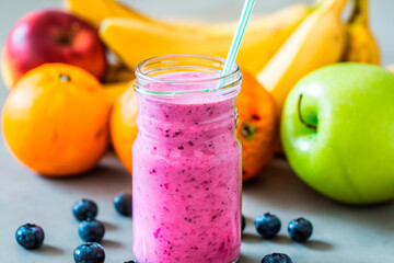 Homemade antioxidant summer fruits smoothie in jar on table with apples, bananas, oranges and blueberries on it
