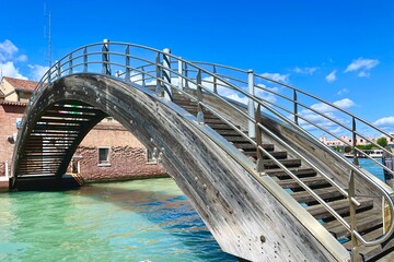 Wooden arched bridge across the strait in Venice under a blue sky
