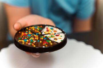 A person holds a homemade chocolate cake with colorful sprinkles
