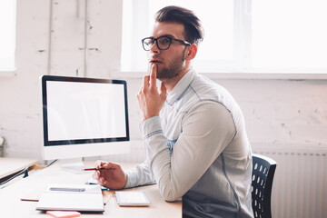 Caucasian serious male it developer pondering on false on website while sitting at desktop with...