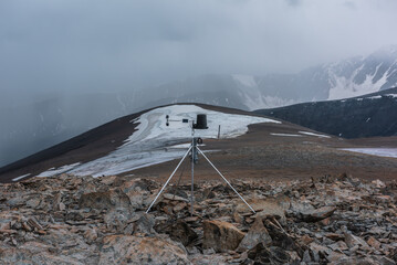 Automatic meteorological station on stone hill with view to large snow-capped mountain range....