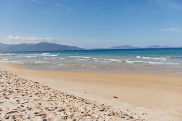 Idyllic Sandy Beach with Mountains and Blue Sky Scenery by the Water's Edge