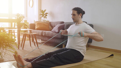 Workout at home concept. Young male doing rows with bands