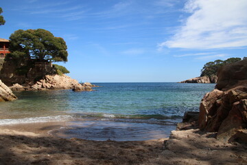 Natural and small coves of the Costa Brava with boats in the background and the blue sky with...