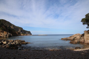 Natural and small coves of the Costa Brava with boats in the background and the blue sky with clouds and blue water. A beautiful place for vacations.