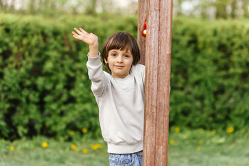 happy little cute boy climbing on children playground, green nature bokeh background.