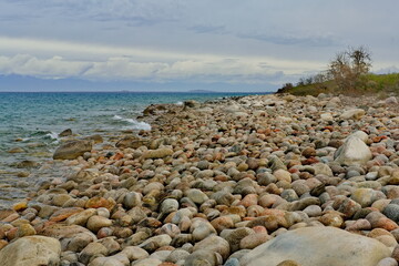 Fototapeta na wymiar Northern Kyrgyzstan. The landscape of the cold Issyk-Kul lake with colored rounded stones of various sizes along the picturesque shore.