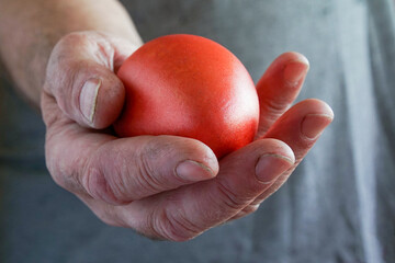 In a man's hand there is a red goose egg.