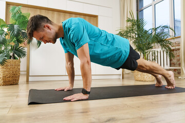 A determined young man maintains a plank position on a yoga mat, focusing on strength and balance...
