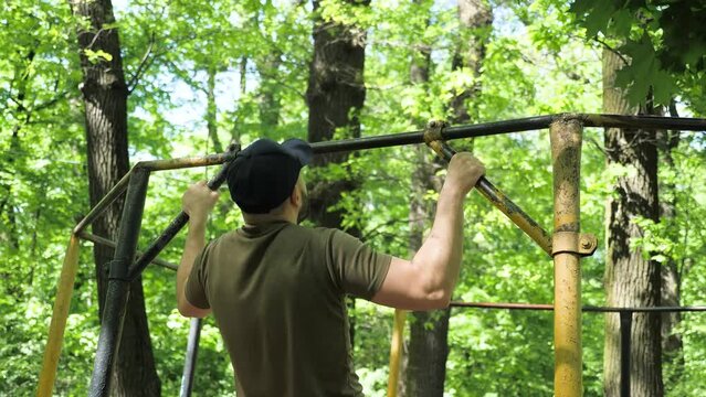 Young Strong Man Doing Clean Pull Ups on Bar in Sunny Park