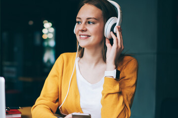 Cheerful female student in headphones enjoying music break after e learning on laptop computer,...