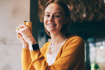 Portrait of cheerful woman feeling excited of photography hobby in cozy cafeteria recalls of beautiful moments, happy hipster girl looking at camera while holding vintage equipment in hands indoors - obrazy, fototapety, plakaty