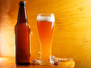 A beer bottle and a glass of wheat beer on a wooden table copy space