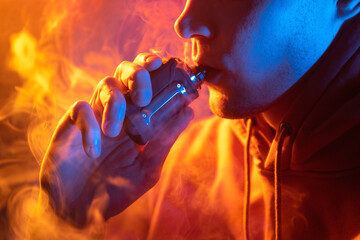 Vaping man exhales a cloud of steam, holding an electronic cigarette. Close-up.
