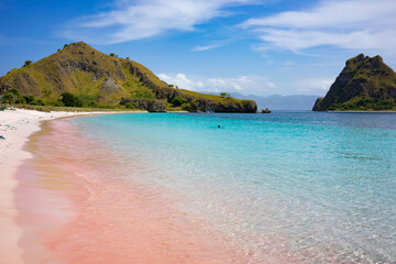 Stunning view of a pink sand beach curving along the vibrant turquoise waters near rugged hills on...