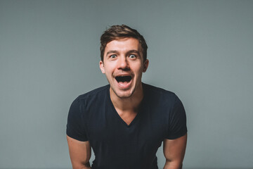 Portrait of a young handsome man on a gray background, a man with his eyes wide open and shouting...