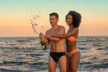 Interracial Couple Popping Champagne on Beach - Romantic Sunset Celebration