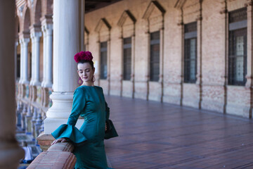 Young, pretty, blonde woman in typical green colored flamenco suit, posing leaning on a brick railing. Flamenco concept, typical Spanish, Seville, Andalusia.