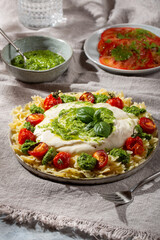 Farfalle pasta with burrata cheese, cherry tomatoes and green pesto on gray background.