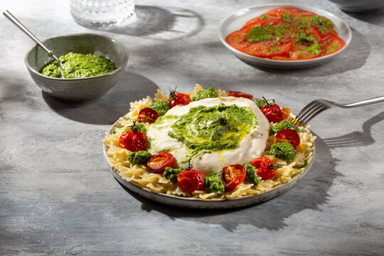 Farfalle pasta with burrata cheese, cherry tomatoes and green pesto on gray background.