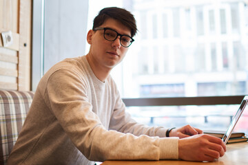 Portrait of successful businessman in stylish eyeglasses working at modern computer connecting to wireless internet while looking at camera.Handsome it professional sitting at table with laptop device